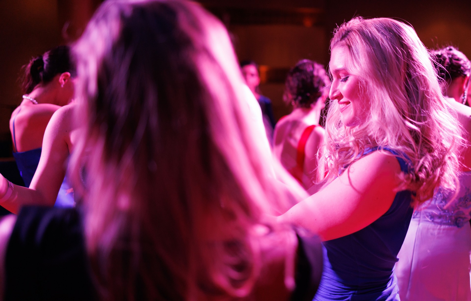 Beautiful young blonde woman dancing among friends in a club, smiling under the bright neon lights